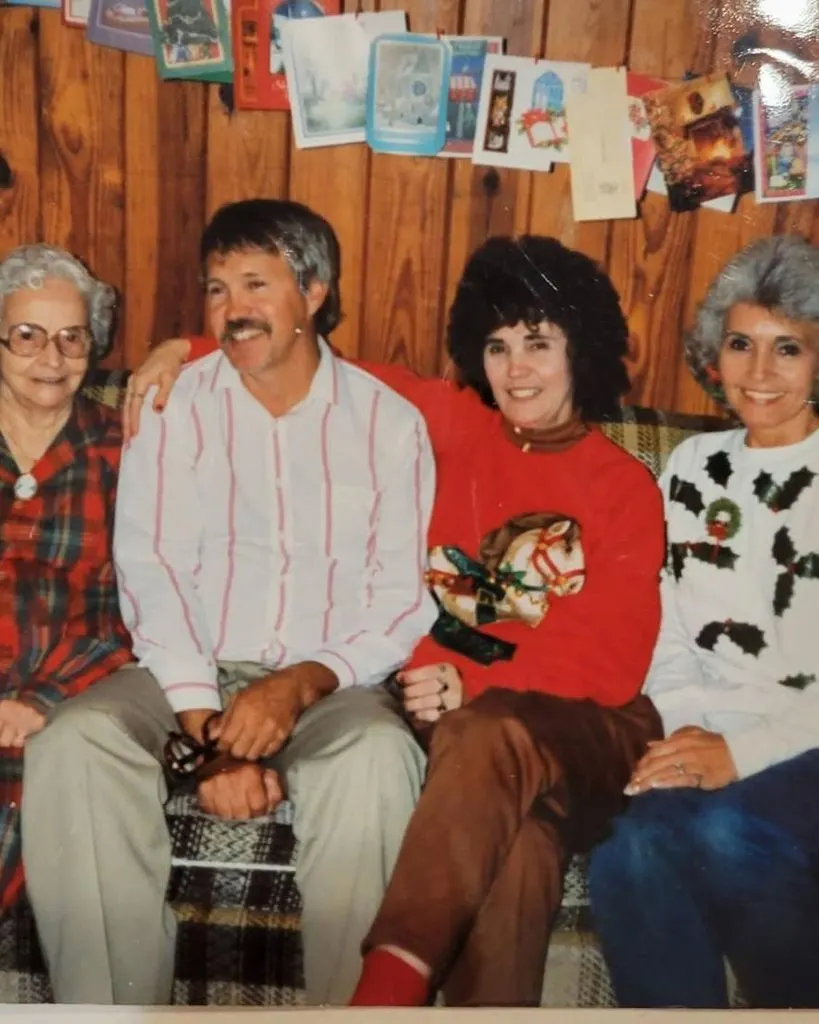 A younger Dagwood with a mustache on a couch under a wall of Christmas cards, with family beside him