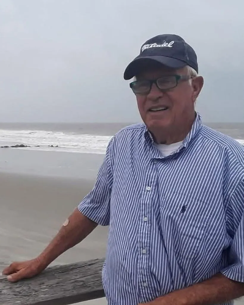 Dagwood McClellan in a Citadel cap and striped shirt, one hand on a railing with the ocean behind him