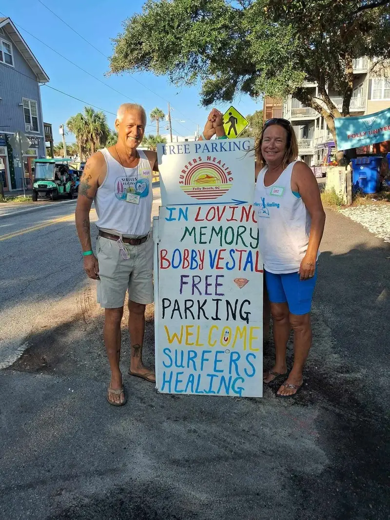Andy and Tara holding a hand painted sign offering free parking to Surfers Healing families
